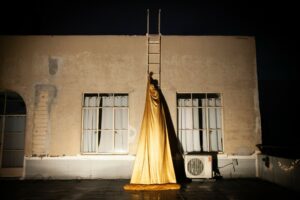 Dancer wearing a gold cloak and climbing a ladder