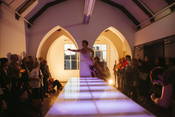 Audience watches dancers holding a female dancer over a light-up table.